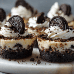 Mini Oreo cheesecake bites topped with whipped cream, crushed Oreo cookies, and mini Oreo halves on a marble serving board.